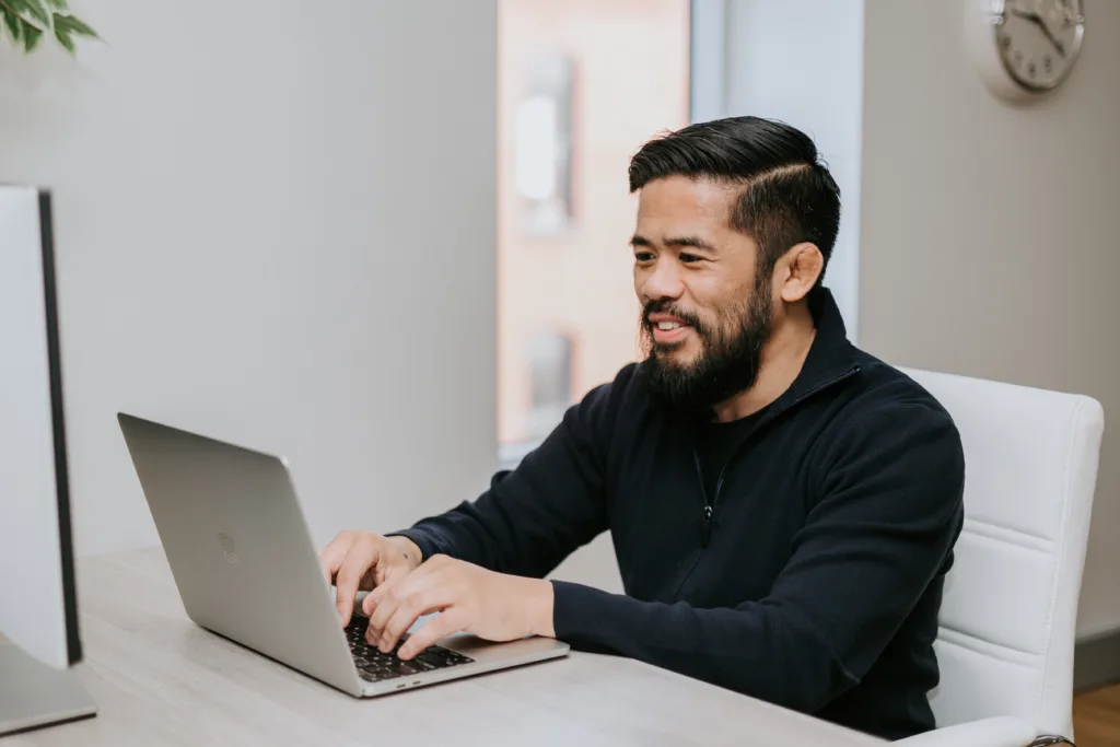 A man sitting at a computer typing at at the beginning of his employee life cycle. 