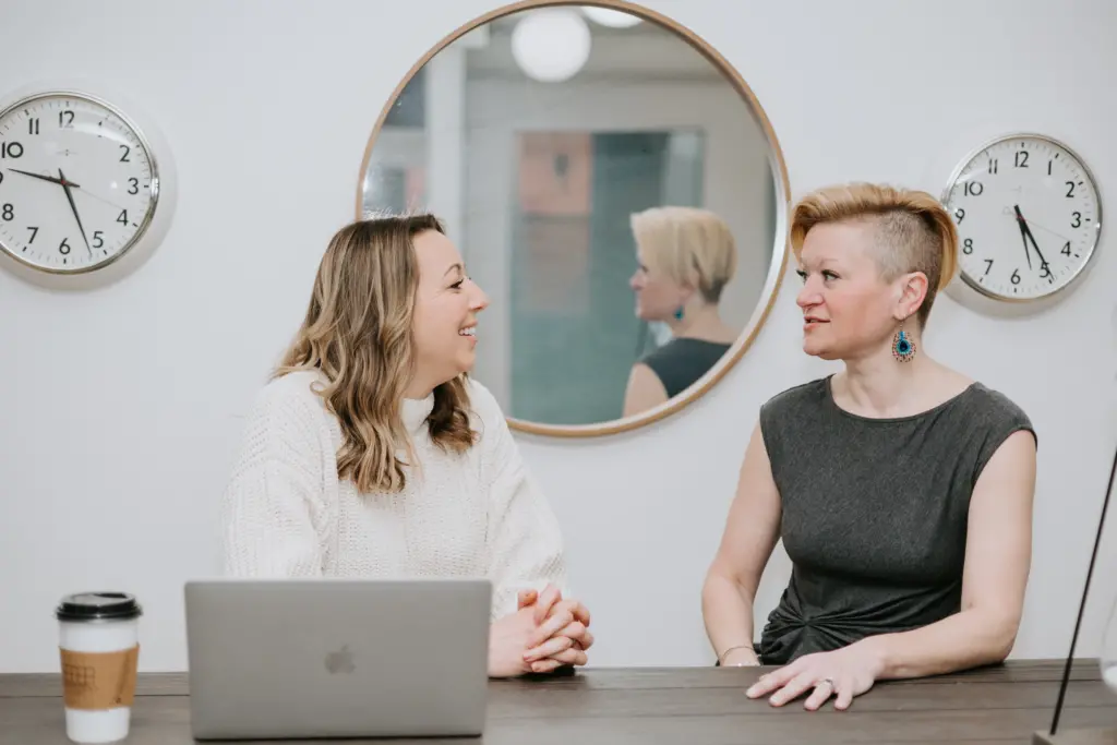 Two women sitting at a table in deep discussion during a micro-mentoring session in an office.