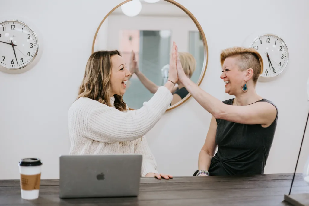 Two woman in an office high-fiving and smiling in celebration of a successful mentor-mentee relationship. 