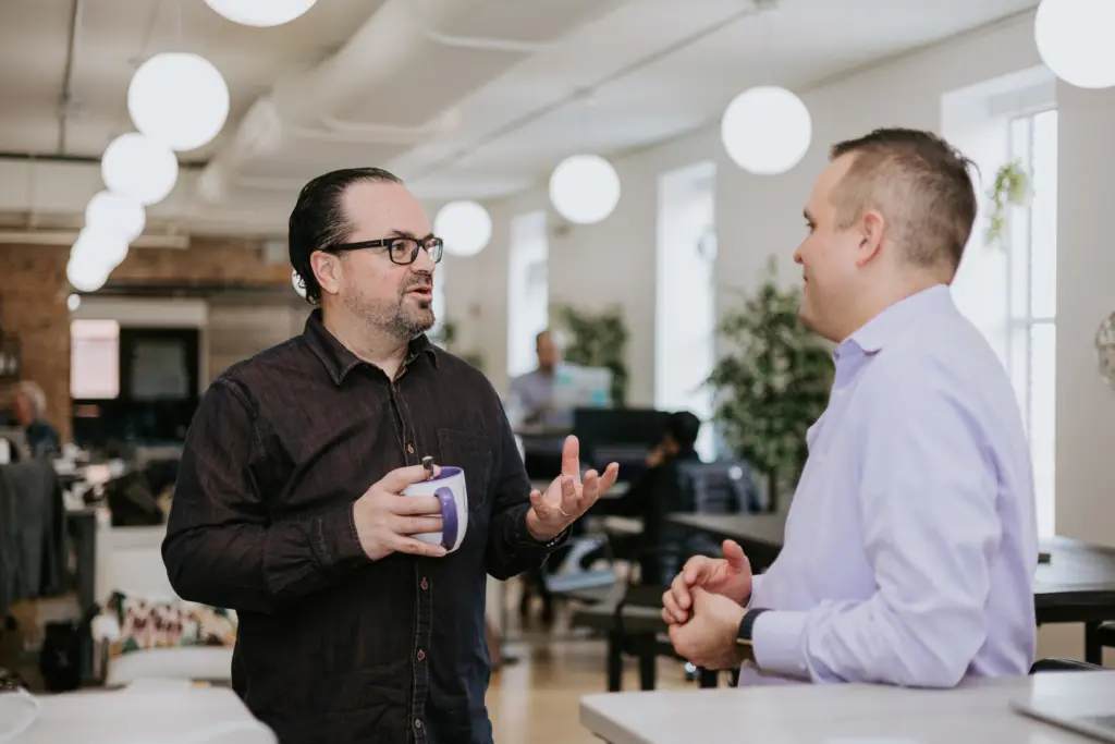 Performance coaching meeting between two men standing in an office chatting.