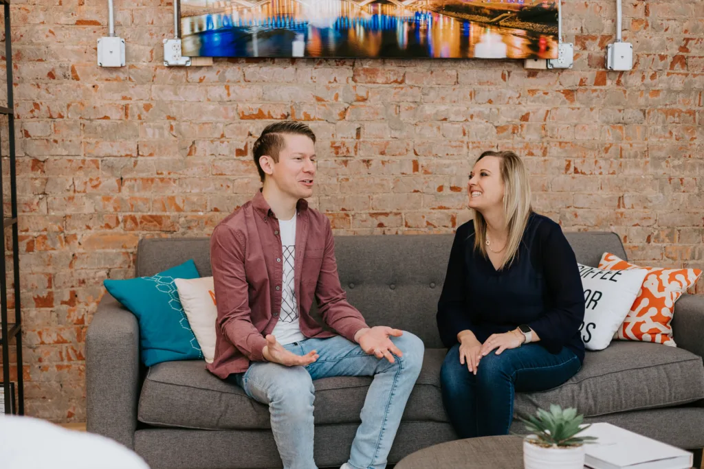 A man and a woman sitting on a couch in discussion about workplace engagement.