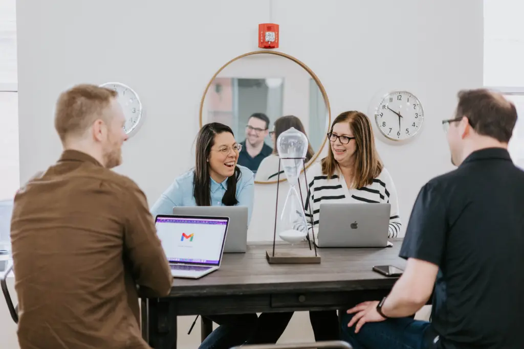 Workers sitting at a table engaged in collaborative employee development with laptops open.