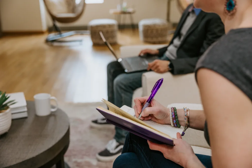 Woman writing in a notebook during a meeting in a lounge. 