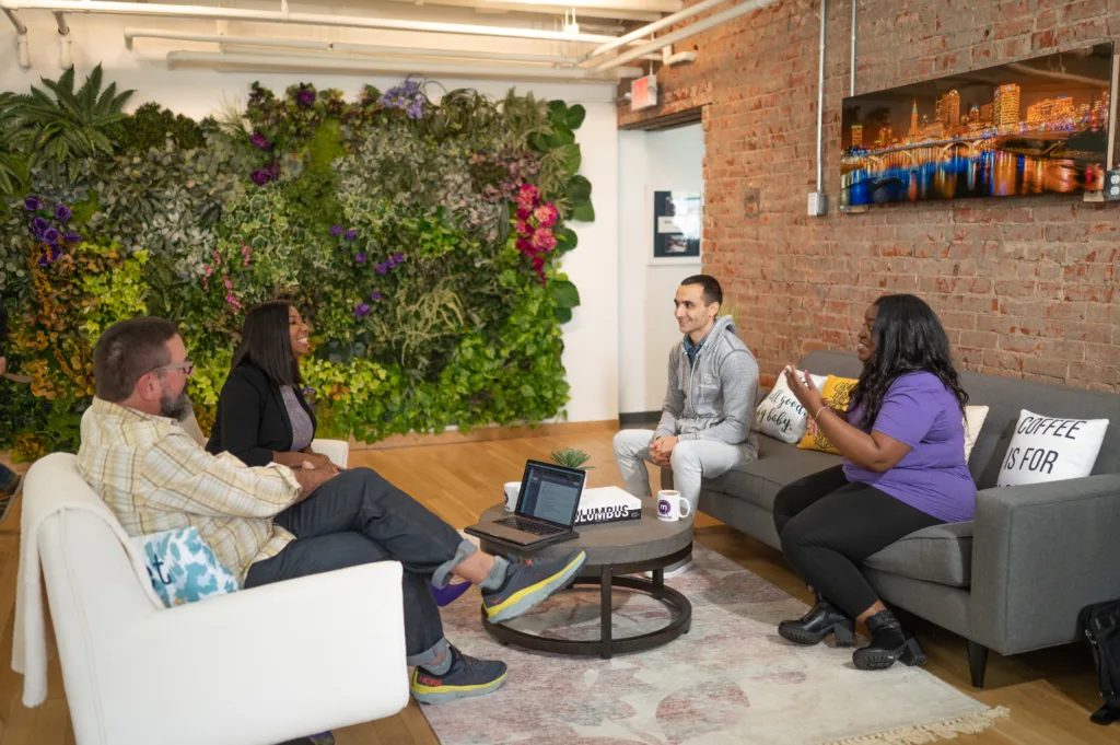 Employee development in an office with 4 employees sitting on coaches and chairs.