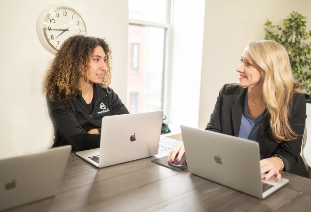 Image of two female employees around a table planning development for different types of mentoring programs.