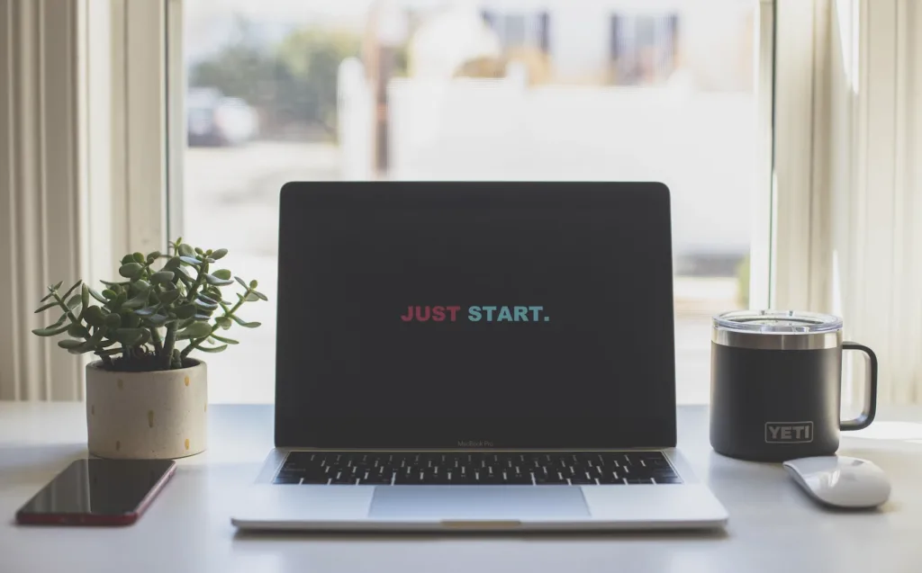 Home office setting with a laptop computer with the words "Just Start" on the screen.