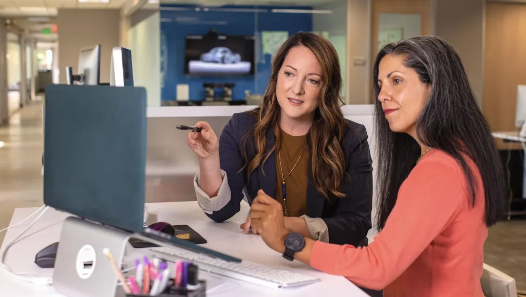 Women working together at a computer on a definition of mentee.