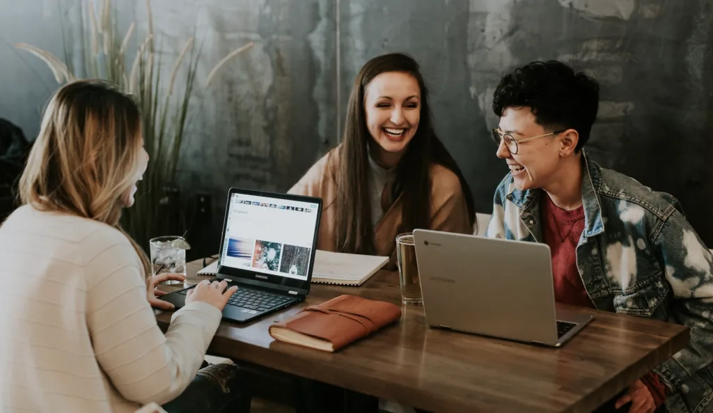 Three work colleagues networking and working on their laptops in a casual office setting.