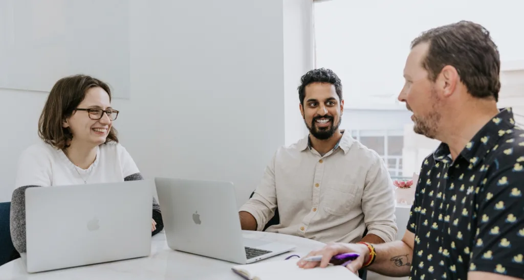 A woman and two men engagemed in a talent development session in an office with computers. 