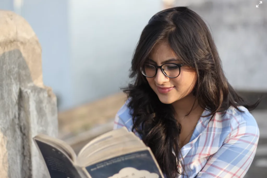 A woman holding and reading a book outside. 